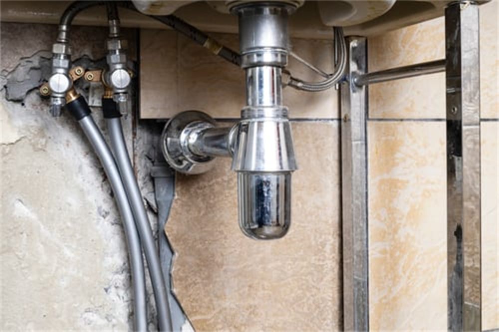 Under-sink plumbing with a chrome P-trap and braided supply lines in a residential Denver, CO home