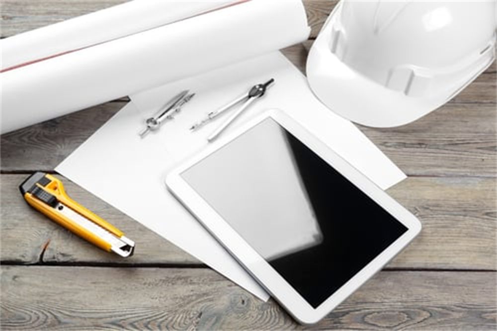 Construction plans, hard hat, drafting compass and tablet laid out on a workbench