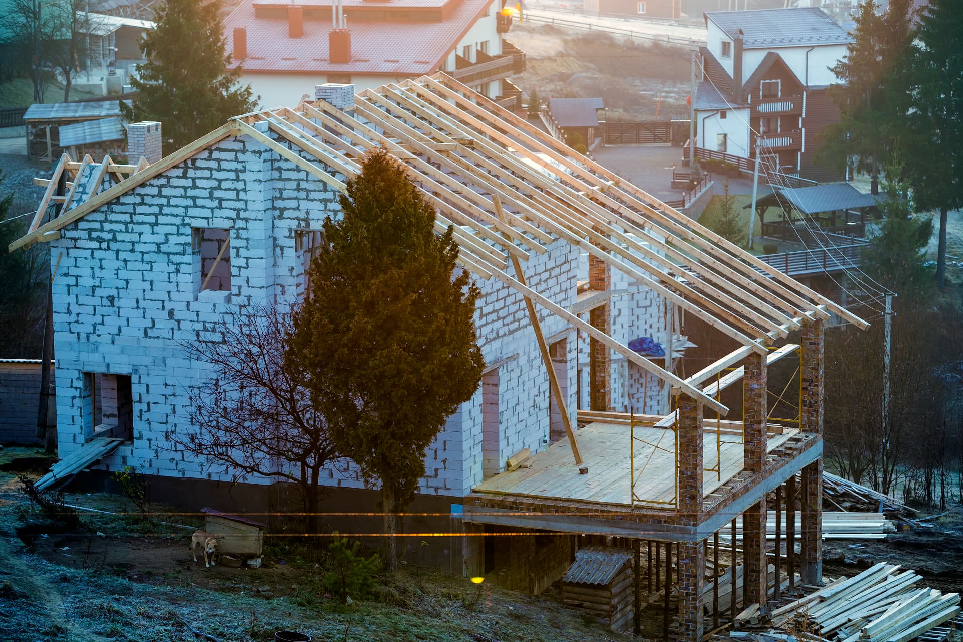 New home under construction with roof framing and block walls at sunrise