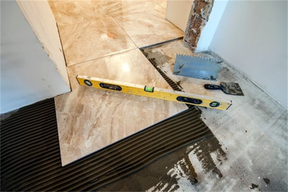Large-format porcelain floor tile being set with a notched trowel and level during a Denver, CO tile installation